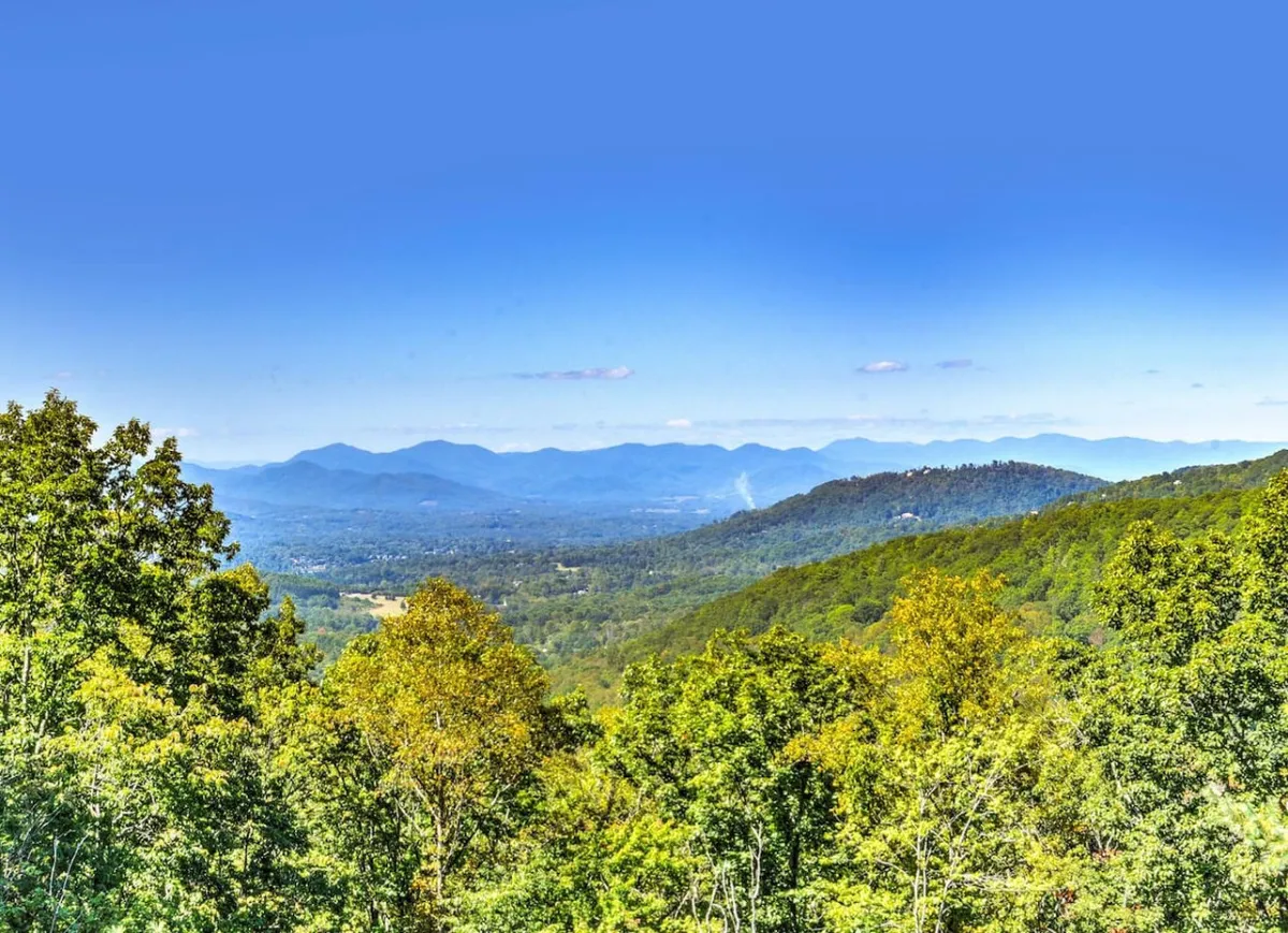 This image presents a sweeping view of the Blue Ridge mountains, framed by lush greenery and a wide expanse of blue sky. The tranquil scene is inviting for relaxation, nature photography, and quiet contemplation. The vantage point evokes the feeling of stepping onto a private terrace to soak in the panoramic scenery.