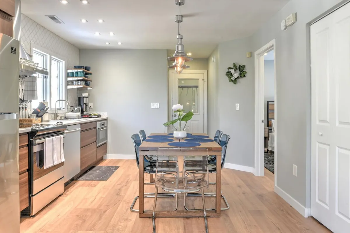 A cozy dining table set near a window, with modern kitchen appliances visible in the background. The space is filled with natural light, creating a warm and functional environment ideal for sharing meals or enjoying morning coffee.