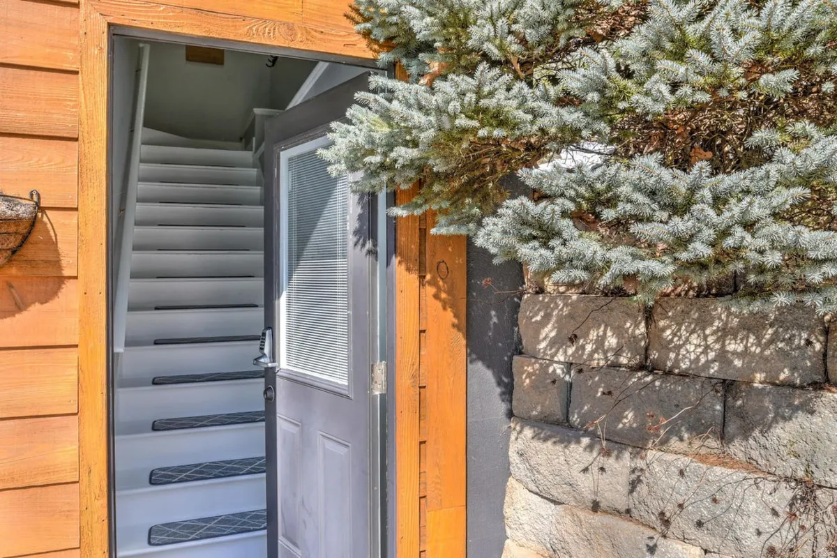 This image shows the entrance door to the home, framed by lush surrounding foliage and a staircase leading upward. The scene suggests the transition from the outdoors to the indoors and highlights the welcoming experience of returning after a day of adventure.