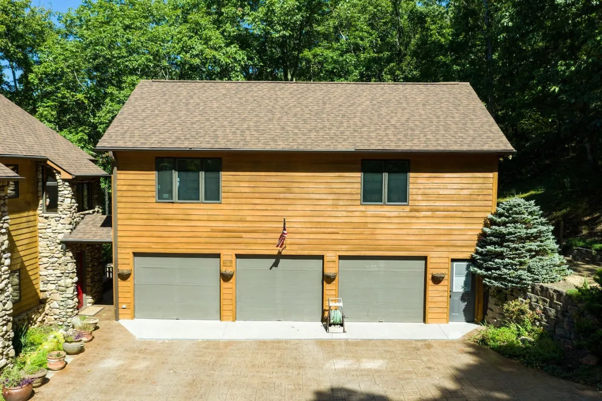 Showing the cottage's wooden exterior with large windows, garage doors, and charming landscaping, this image captures the inviting entry to the home. The scene hints at the transition from the comfort of the interior to the outdoor experiences described in the section, and the welcoming mood invites guests to imagine stepping outside onto the terrace.