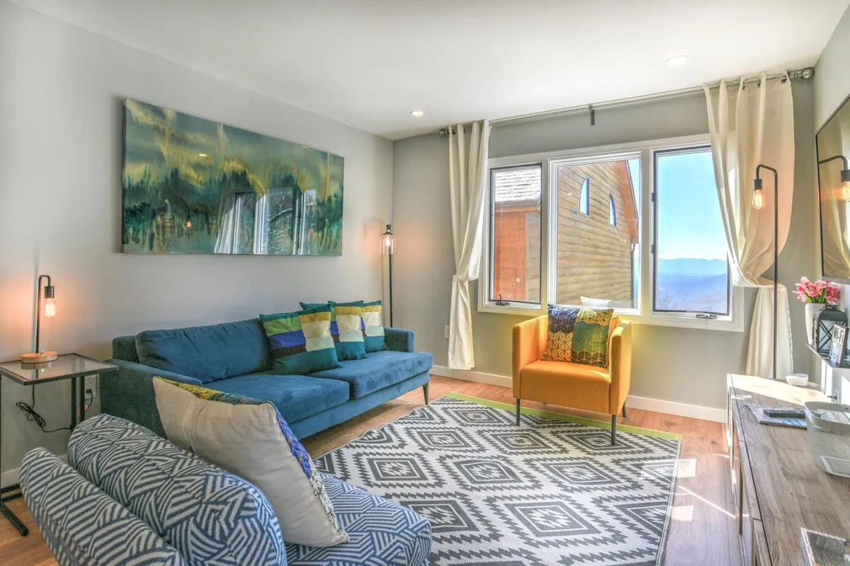A comfortable living space with a bold blue sofa, an orange accent chair, vibrant geometric rug, and eye-catching wall art. Morning light pours through a nearby window, illuminating the plush furnishings and creating a cozy nook for reading or conversation.