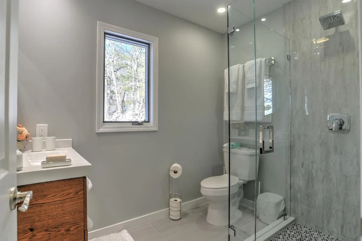 A modern ensuite bathroom with a glass shower enclosure, a sleek vanity with sink, and natural light streaming through a window. The clean lines and contemporary finishes evoke a spa-like atmosphere, ideal for rejuvenation.